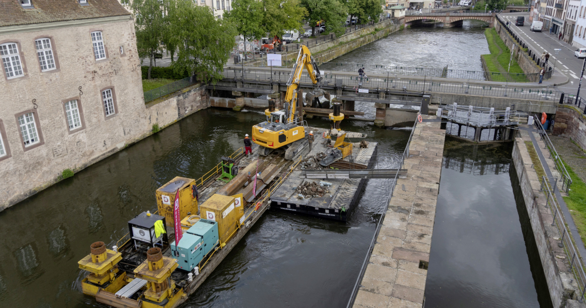 Le tirant d’air sous les ponts étant trop faible pour une amenée par voire d’eau, le grutage de la pelle sur le ponton s’est imposé.