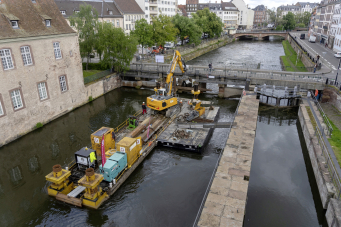 Le tirant d’air sous les ponts étant trop faible pour une amenée par voire d’eau, le grutage de la pelle sur le ponton s’est imposé.